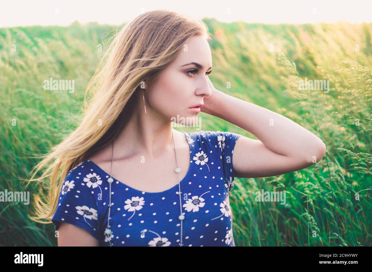 Girl blonde in a blue short tight dress sit in tall grass Stock Photo