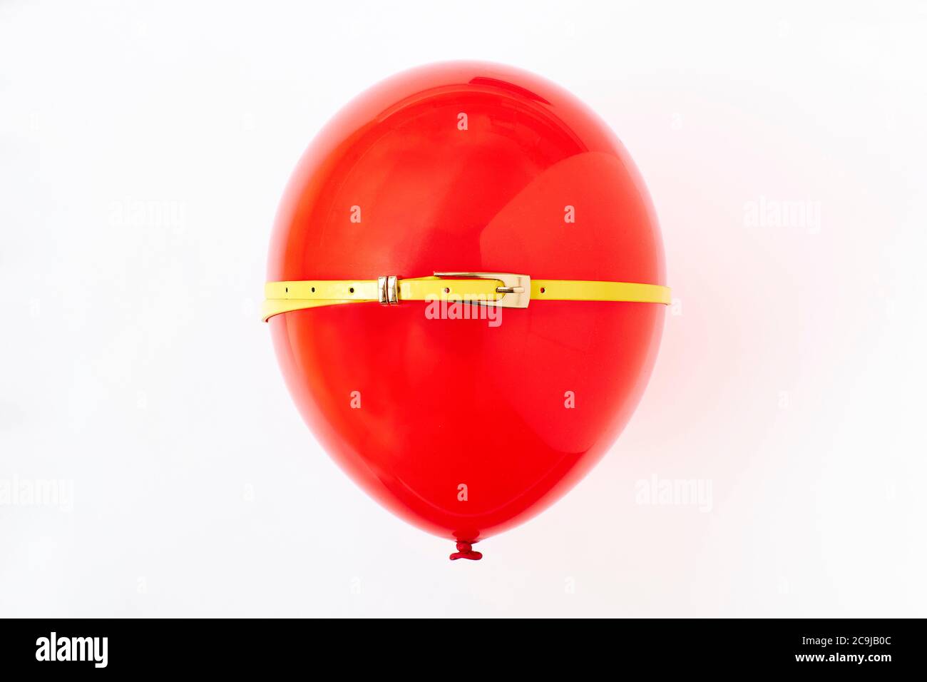 Red balloon with yellow belt, conceptual image of bloated stomach. Stock Photo
