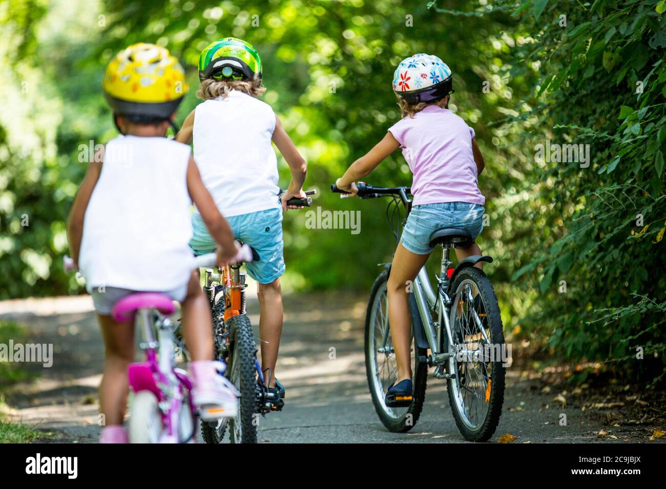 Children wearing helmets and cycling in park. Stock Photo