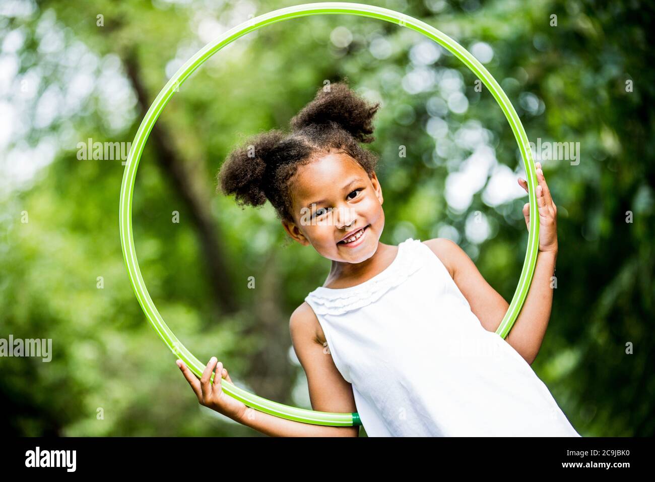 Girl playing with hula hoop in park, smiling, portrait. Stock Photo