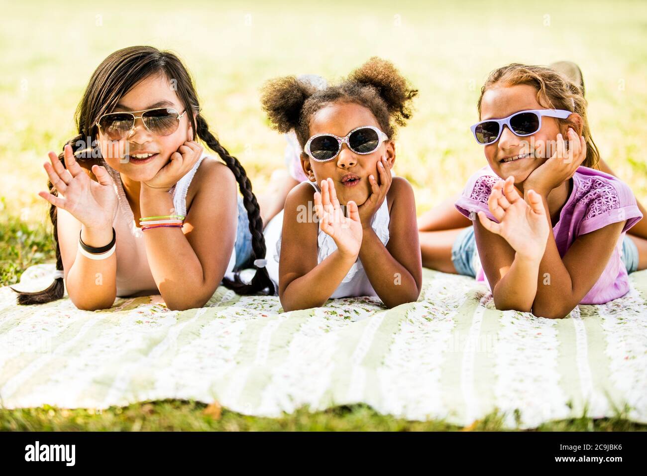 Girls wearing sunglasses and lying side by side on blanket in park, smiling, portrait. Stock Photo