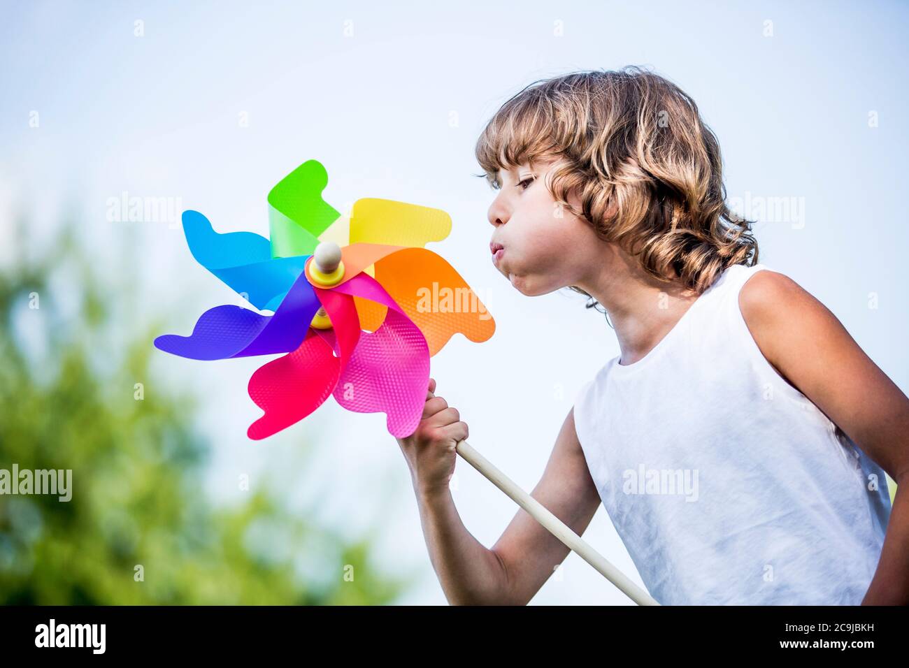 Boy blowing colourful paper windmill in park. Stock Photo