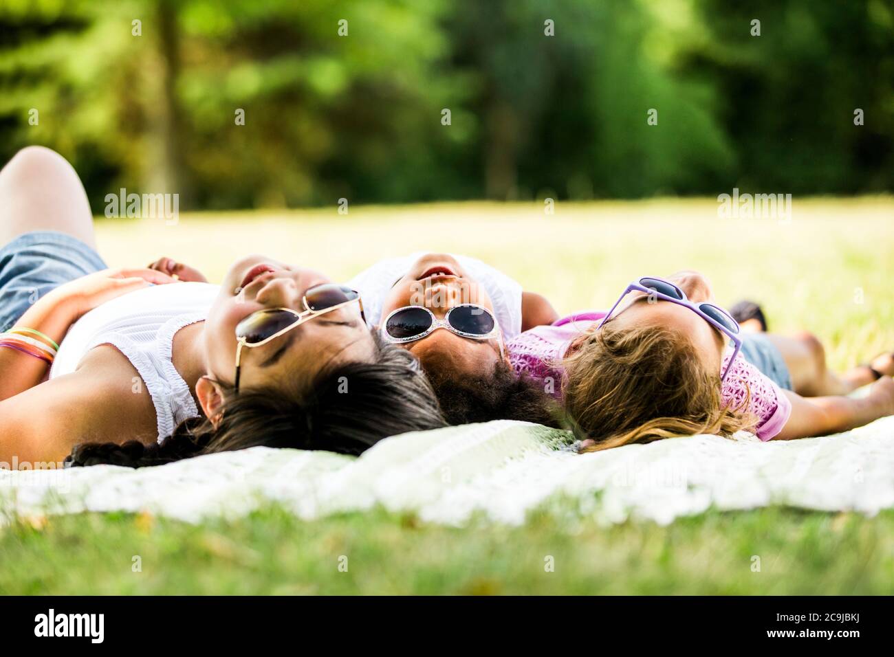 Girls wearing sunglasses and lying side by side on blanket in park. Stock Photo
