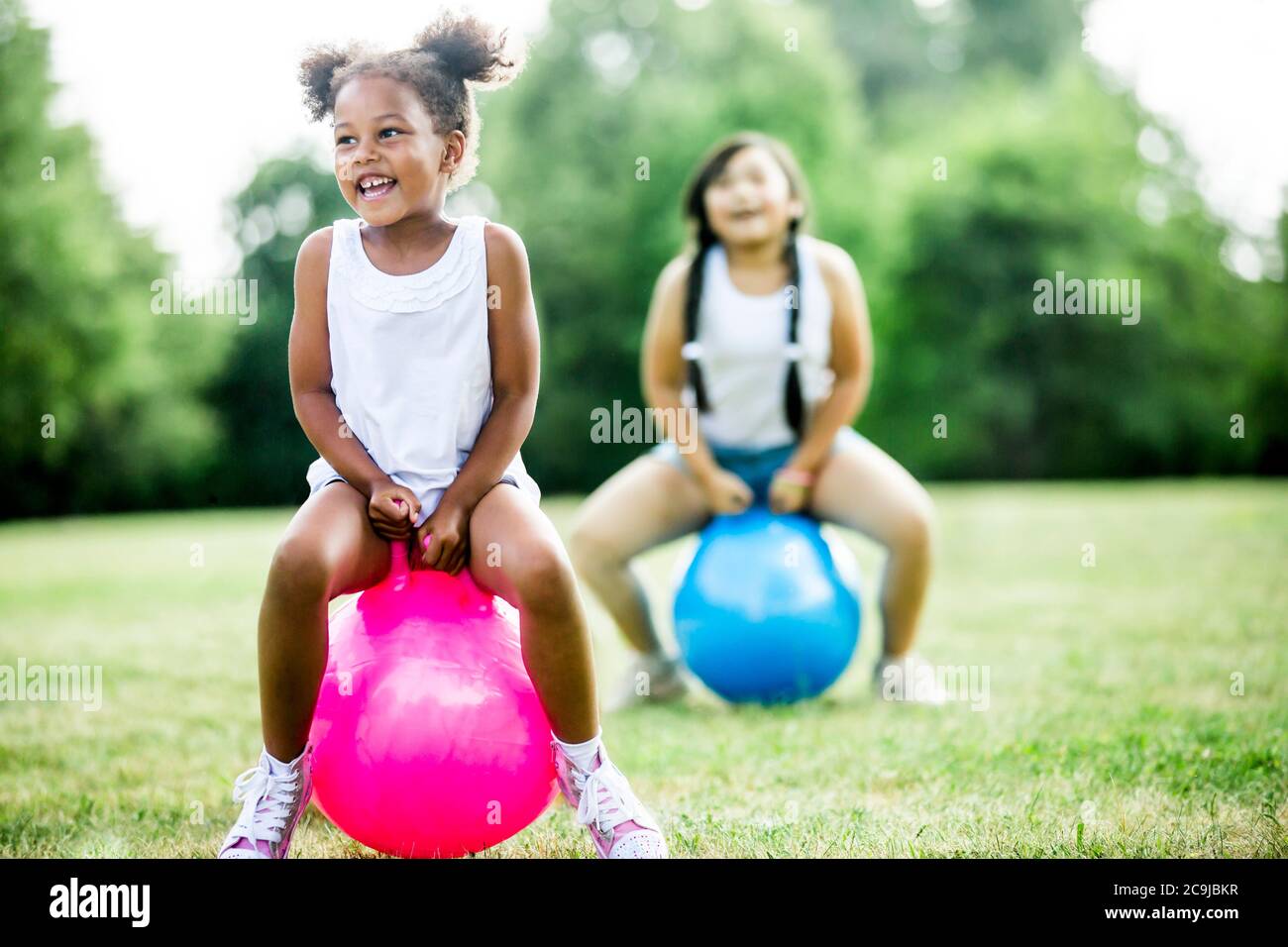 Girls bouncing on inflatable hopper in park, laughing. Stock Photo