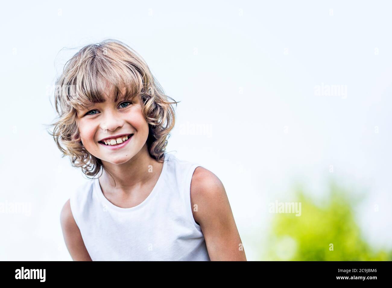 Boy with blonde hair smiling in park, portrait. Stock Photo