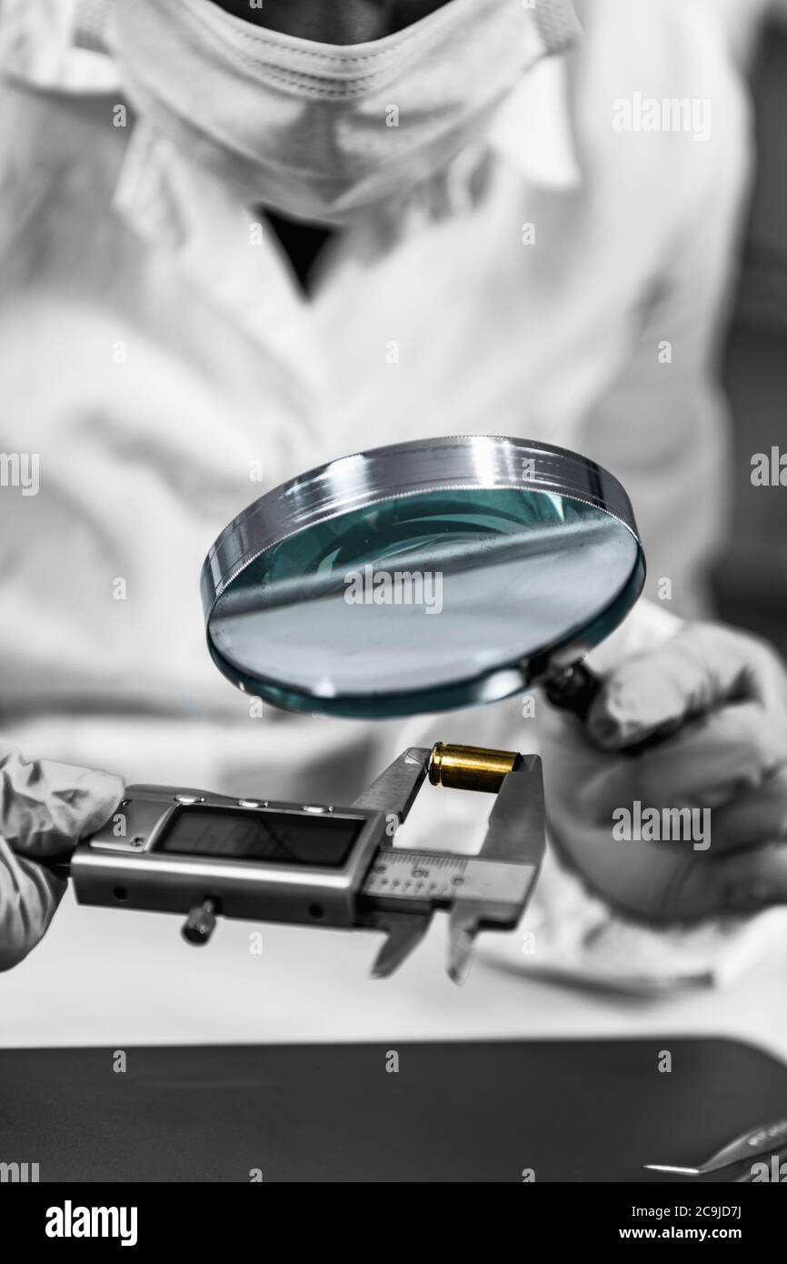 Forensic science analyst using magnifying glass, examining bullet