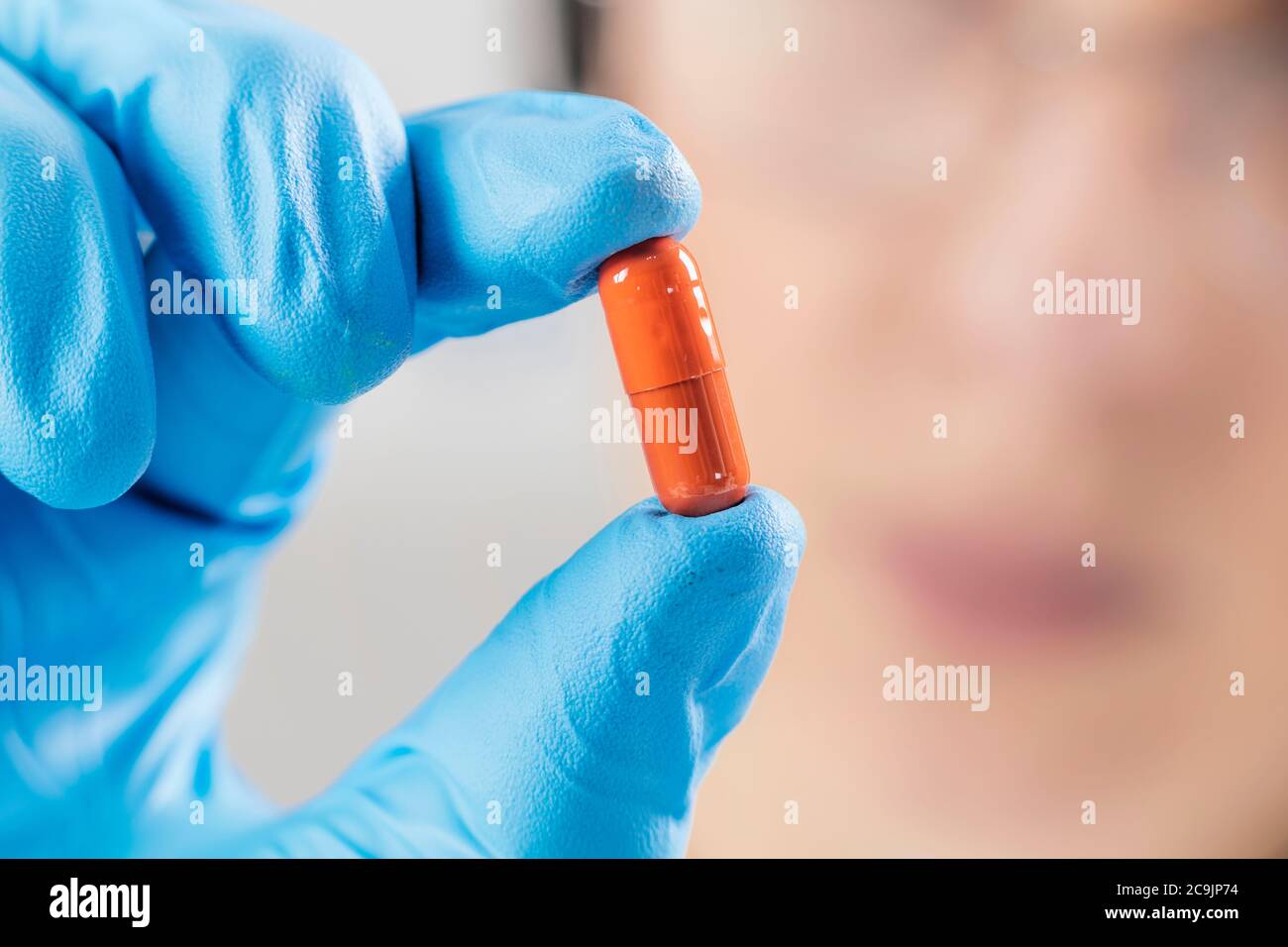 Scientist hand in glove holding orange pill with blue glove in laboratory. Stock Photo