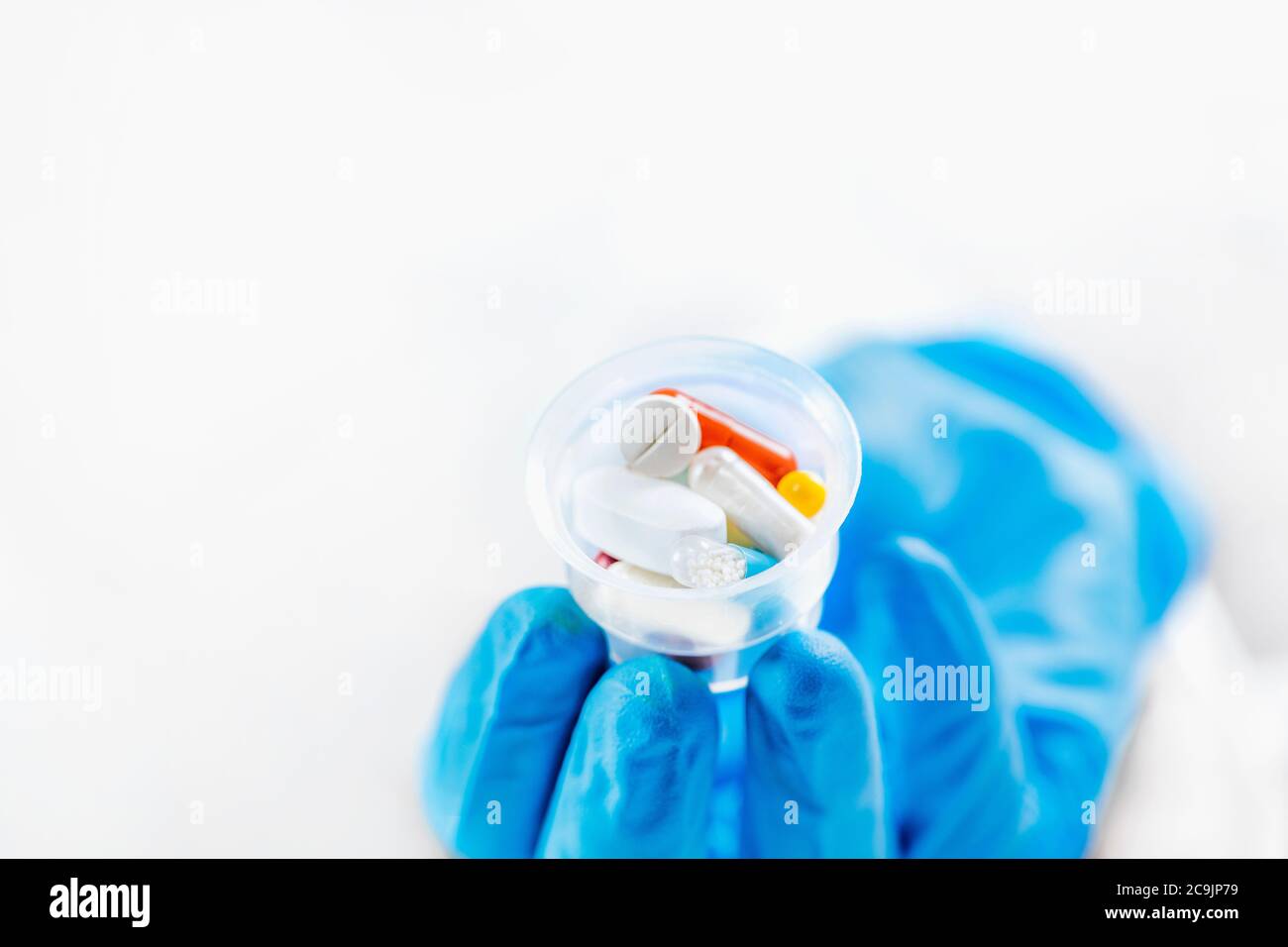 Female doctor's hand In blue glove holding graduated medicine cups full of pills. Copy space and white background. Stock Photo