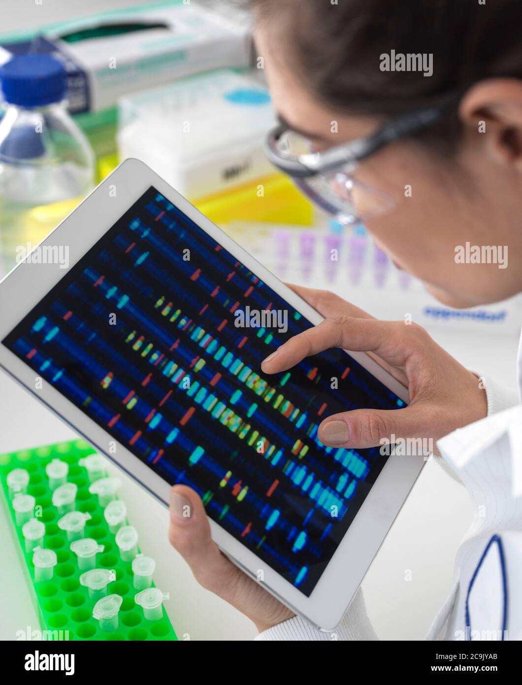 Scientist viewing DNA (deoxyribonucleic acid) profiles on a touch screen tablet during a genetic experiment. Stock Photo