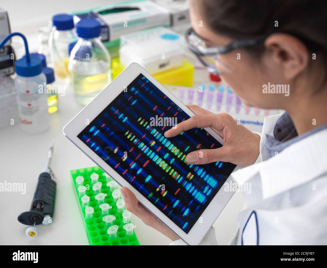 Scientist viewing DNA (deoxyribonucleic acid) profiles on a touch screen tablet during a genetic experiment. Stock Photo
