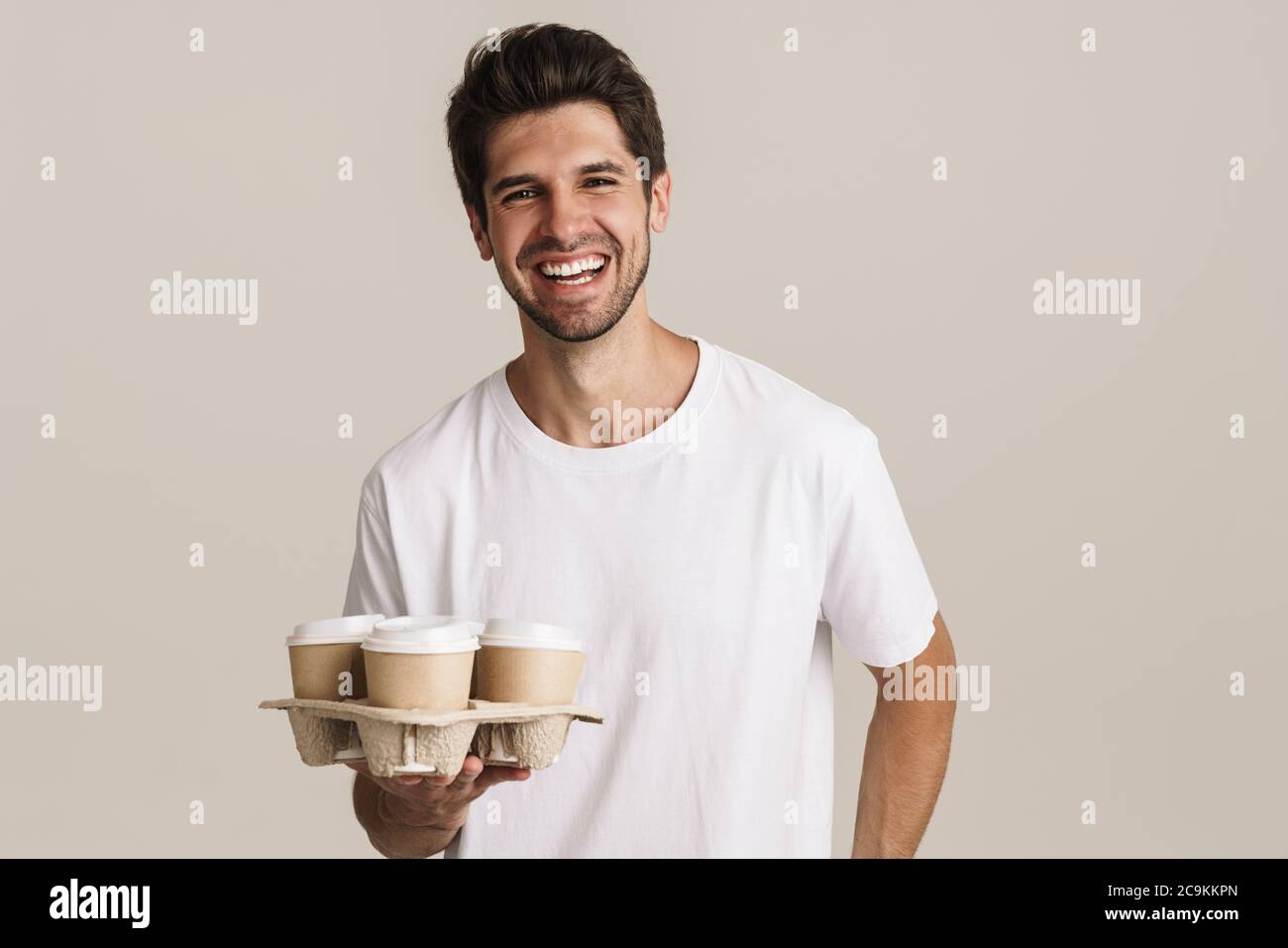 Portrait of cheerful handsome man laughing and holding paper cups ...