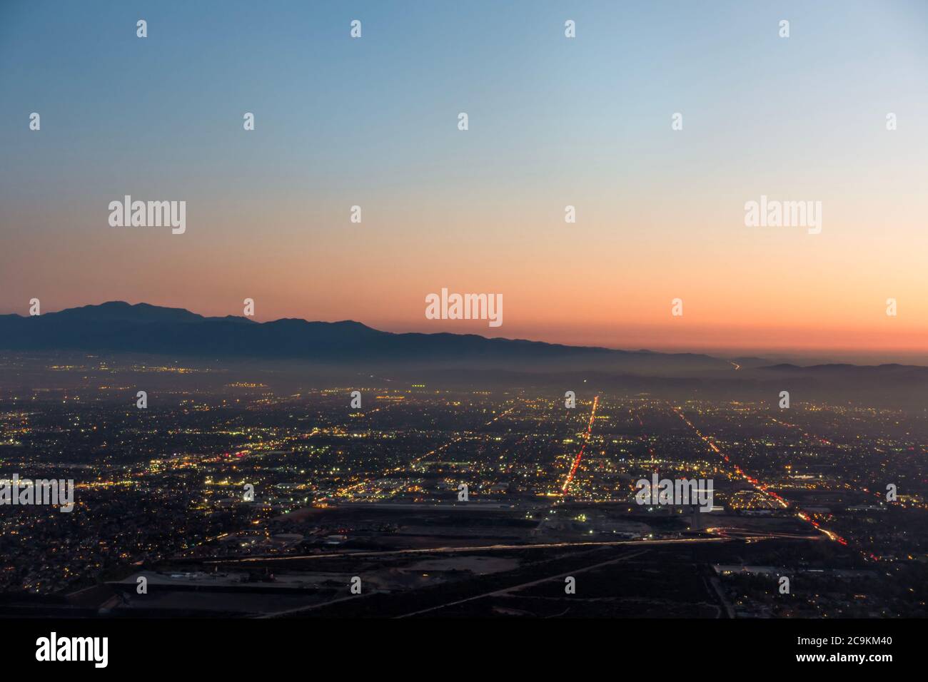 The city lights of the skyline of the Inland Empire near Los Angeles California begin to appear as the sun sets in a dramatic orange sunset. Stock Photo