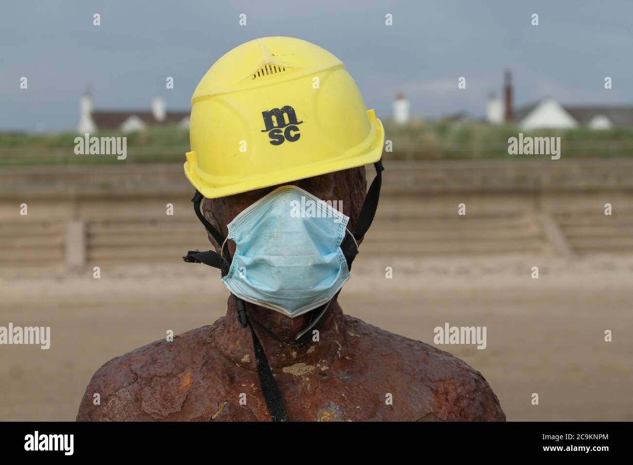 Liverpool, UK. 31st July, 2020. One of Sir Antony Gormley Iron men draped in a hard hat and a face mask at Crosby Beach.The Government has made it mandatory to wear face coverings in all public transport, supermarkets and indoor shopping centers as a measure to combat the spread of the novel coronavirus. Credit: SOPA Images Limited/Alamy Live News Stock Photo