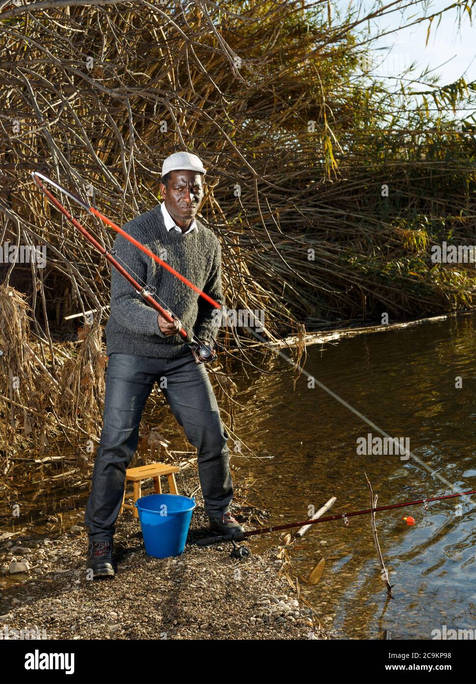 Portrait of afro fisherman standing near river and pulling fish Stock Photo
