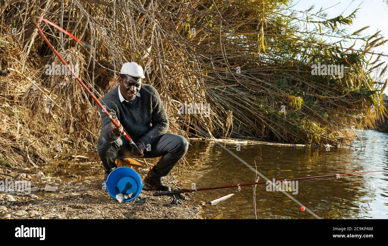 Portrait of afro fisherman sitting on stool and pulling fish Stock Photo