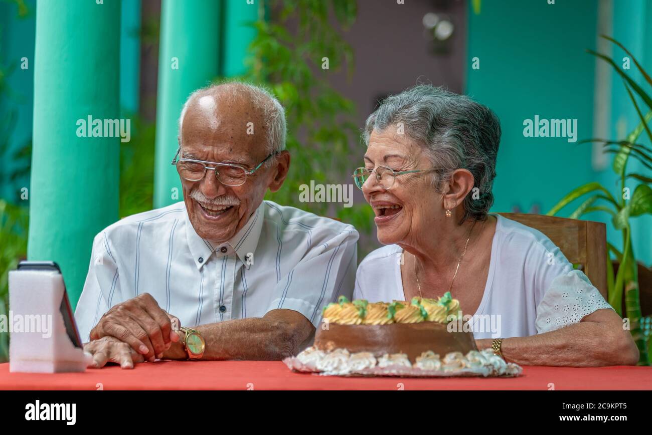 Smiling elderly couple sitting at a table looking at a cell phone Stock Photo