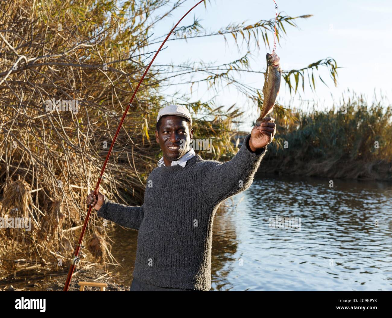 Portrait of afro fisherman holding fishing rod with fish on hook Stock Photo