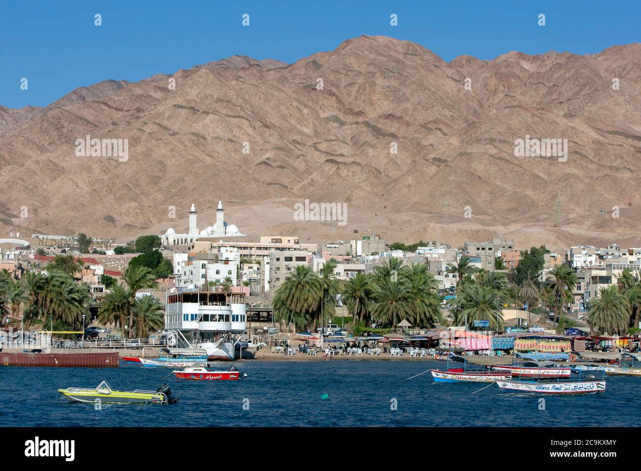 Apartment buildings and restaurants sit on the bank of the Gulf of Aqaba in Jordan. In the background stands a spectacular mountain. Stock Photo