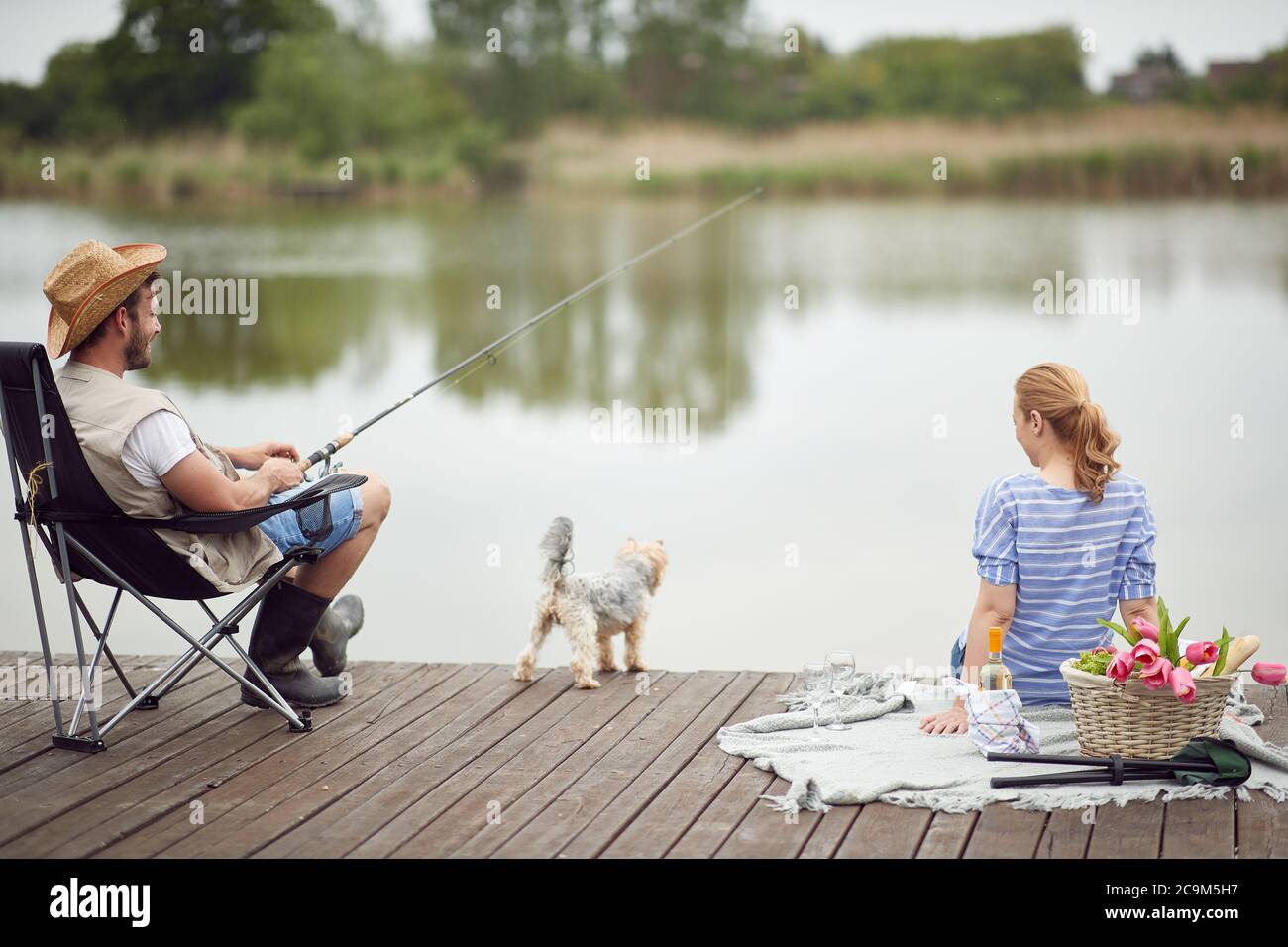 Spouses enjoy fishing and a picnic with their dog on a beautiful day Stock Photo