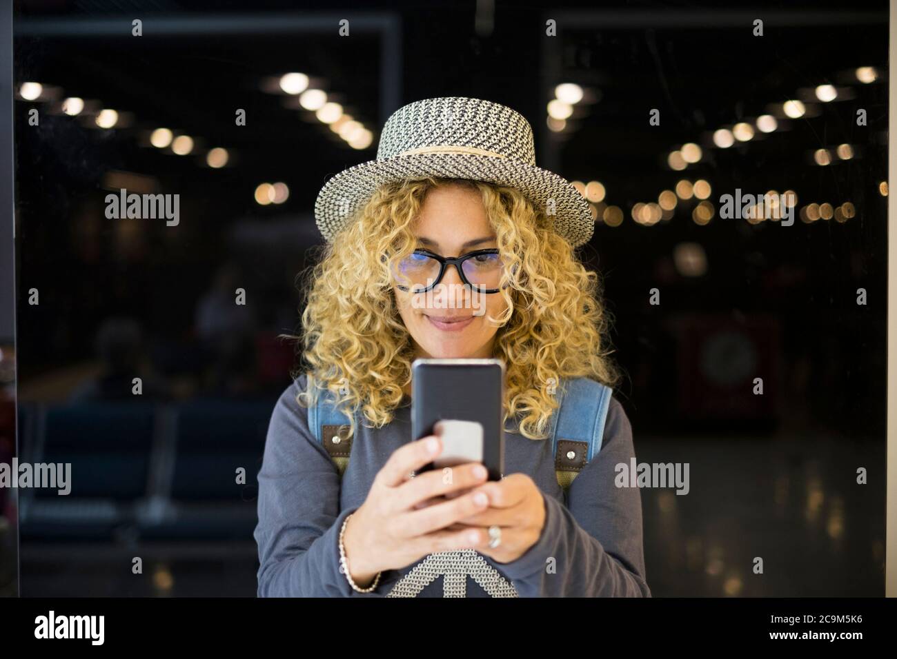 portrait and close up of beautiful curly and blonde woman looking at the camera smiling - happy people traveling at the airport - vacations outdoors Stock Photo