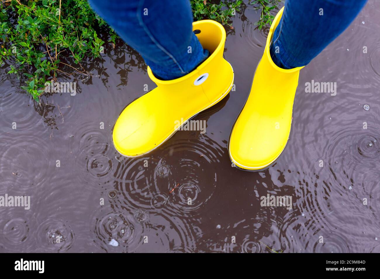 Woman in yellow rubber boots standing in the puddle in rain outdoors ...
