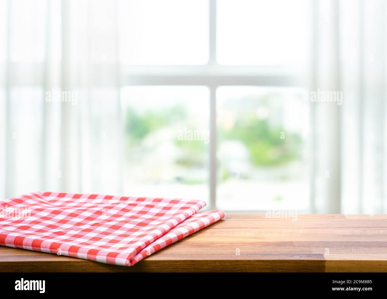 Red fabric,cloth on wood table top on blur window in morning background.For montage product display or design key visual layout. Stock Photo