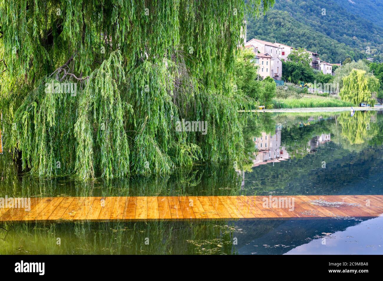 Village and willow reflecting on the lake with the pier submerged in the water. View from the shore of Lago di Lago, Revine Lago, Treviso, Italy Stock Photo