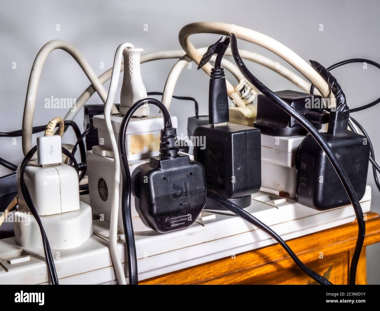 Close shot of a probably unsafe, overloaded 240 volt electricity supply, with a mess of multiple UK plugs, sockets, extensions, wires and cables. Stock Photo