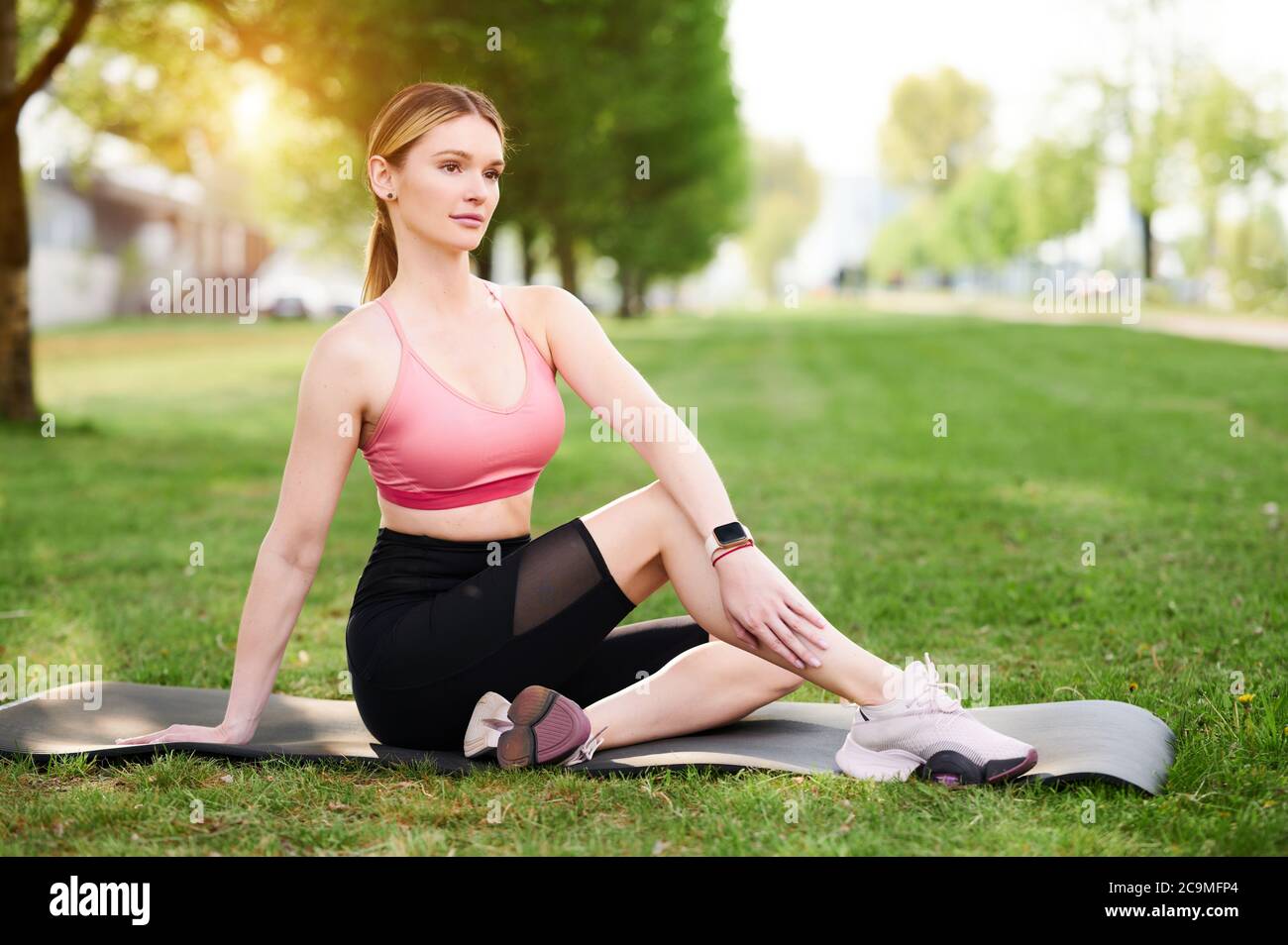 Woman stretching seated spinal twist. Girl practicing yoga, doing Half lord of the fishes exercise, Ardha Matsyendrasana pose in city public park Stock Photo