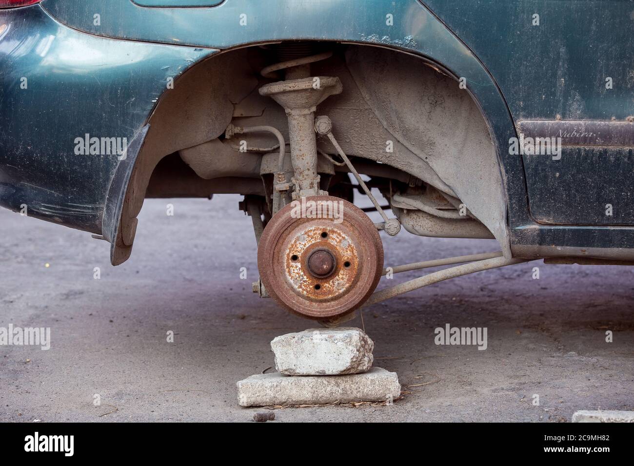 Car without wheels costs on brick, old rusty car brakes in poor