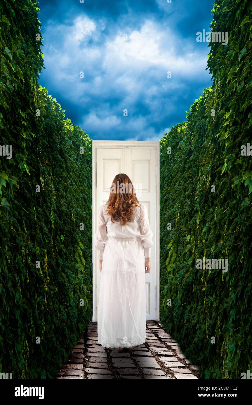 brunette with long hair young woman wearing a white dress, in front of a mysterious white closed door Stock Photo