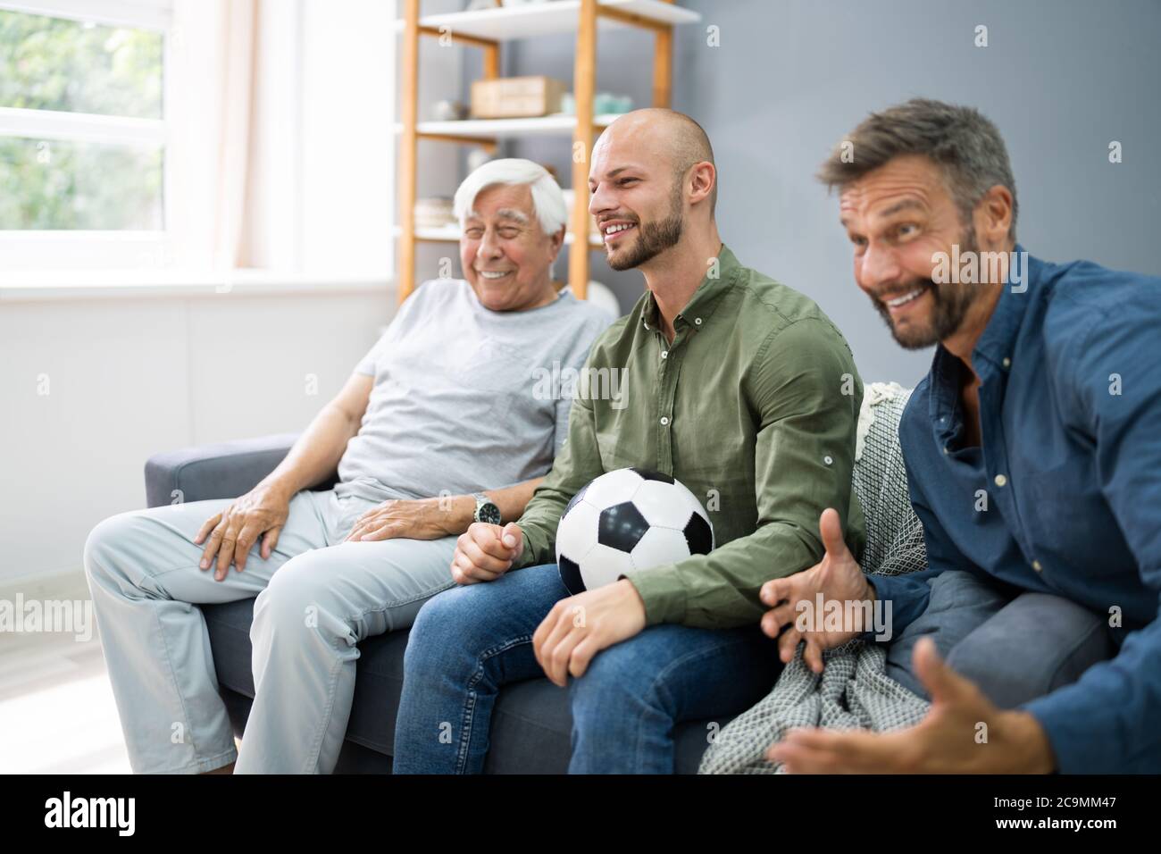 Three Generation Sport Fans Watching Football On TV Stock Photo