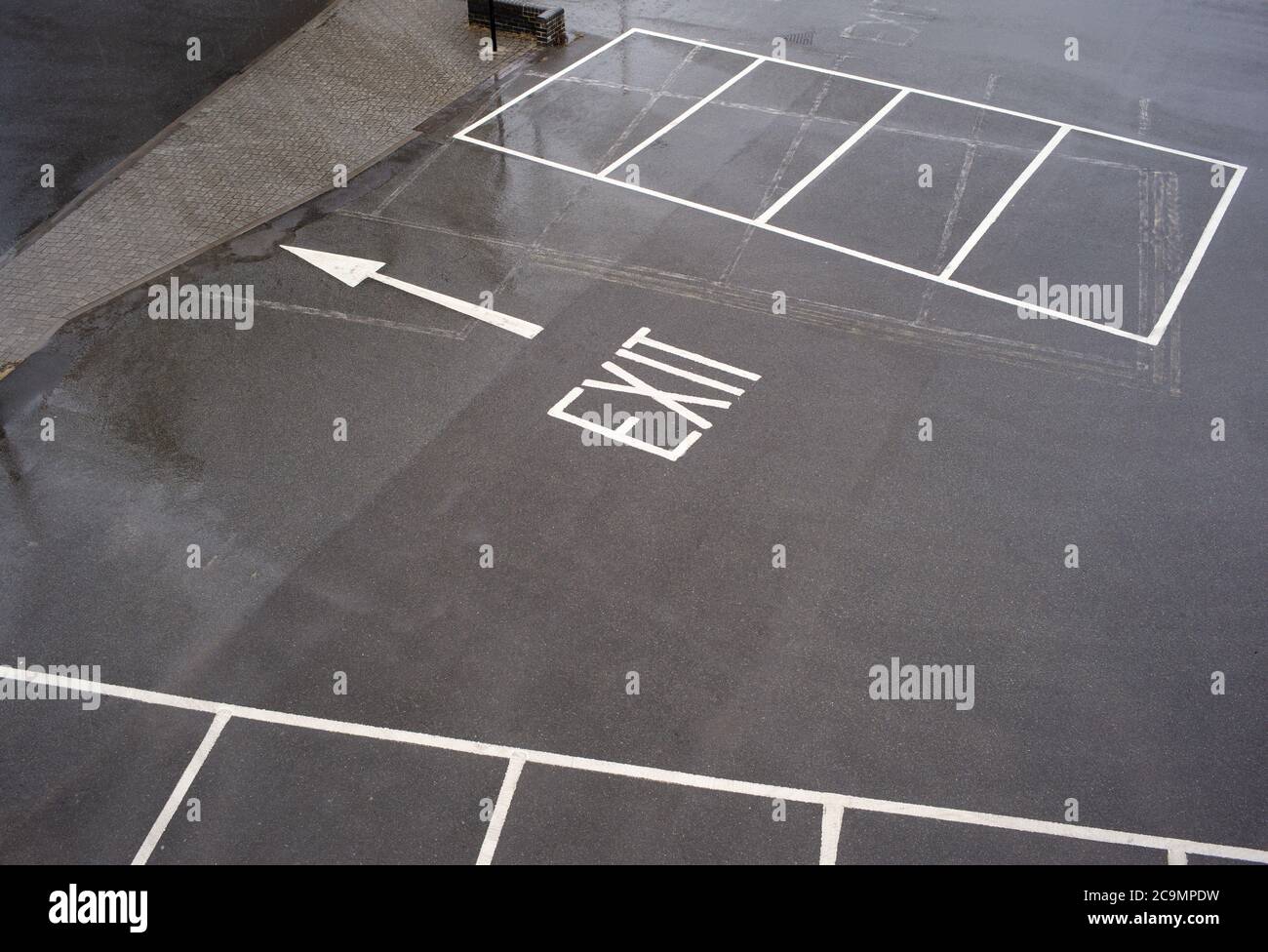 A concept image of an exit sign with an arrow taken from above on the pavement of an outside empty car park showing the exit and empty spaces. Stock Photo