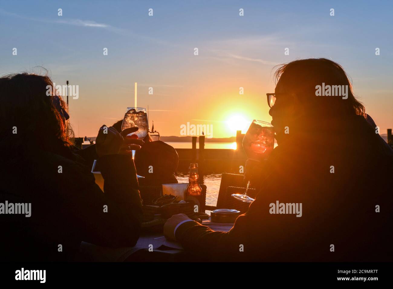 Friends drinking an aperitif in an outdoor cafe on the lakefront at sunset, Bardolino, Lake Garda, Verona, Veneto, Italy Stock Photo