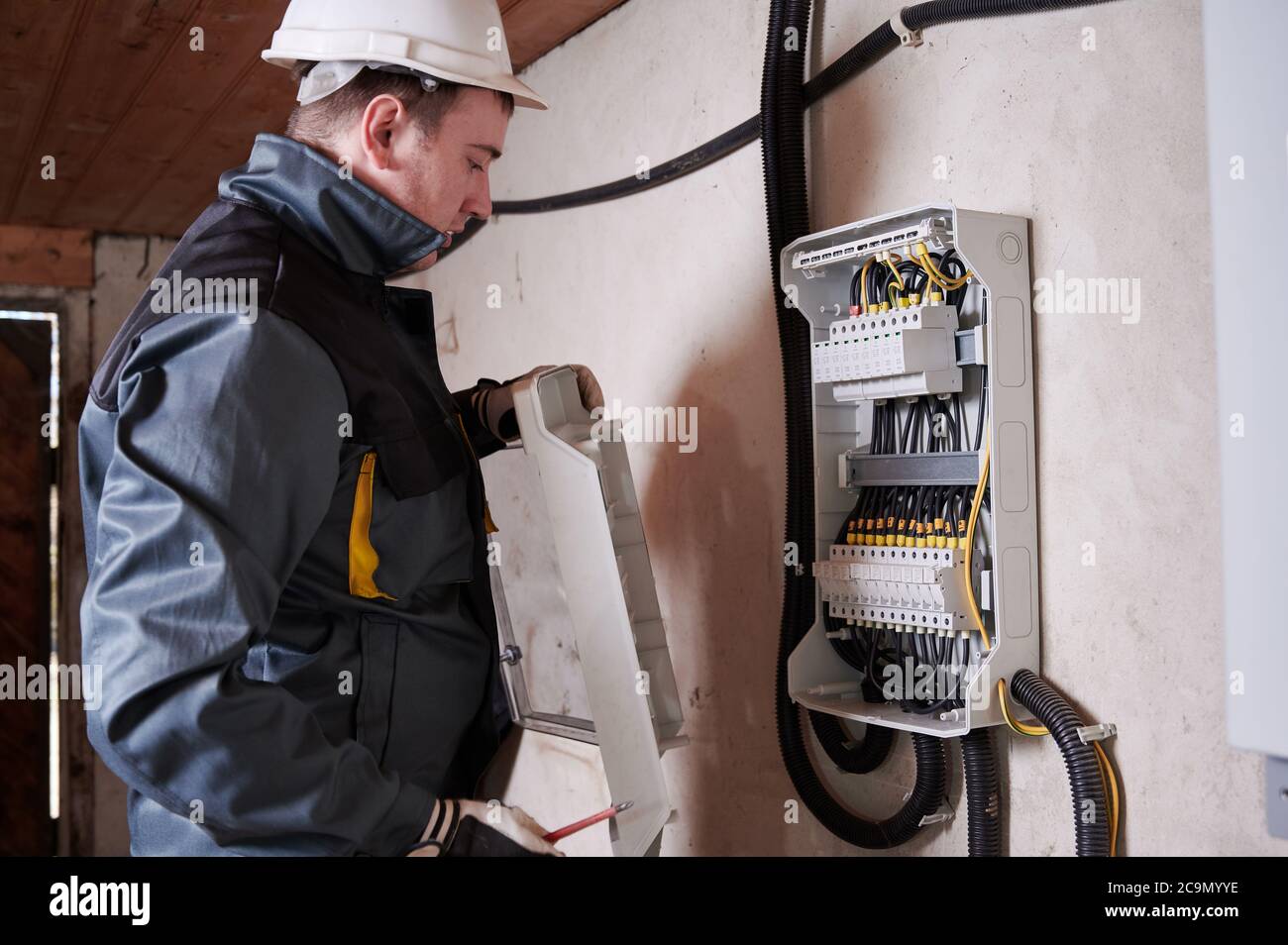 Electrical engineer in work uniform checking electric box with wires