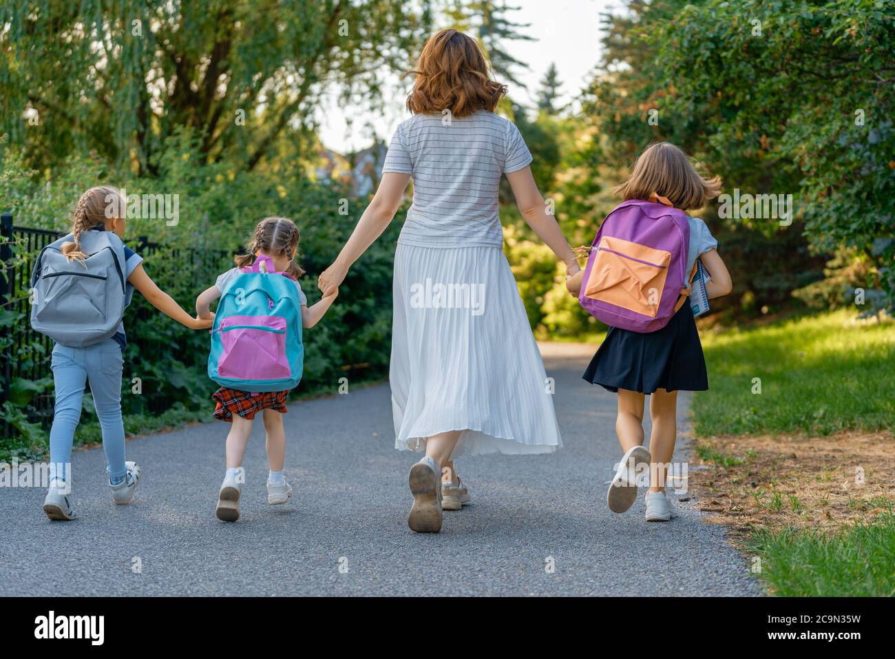 Parent and pupils of primary school go hand in hand. Woman and girls ...