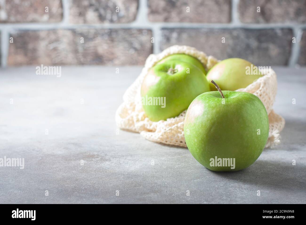Organic green apples in reusable cotton net bag on wooden table. Eco-package, zero waste concept. Selective focus. Stock Photo
