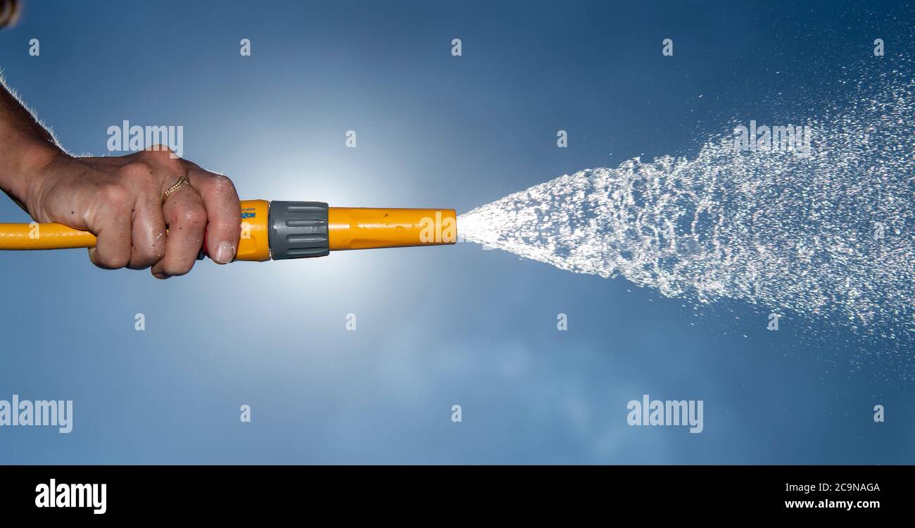 Water from a hose pipe being sprayed under pressure, against a blue summers sky. North Yorkshire, UK. Stock Photo