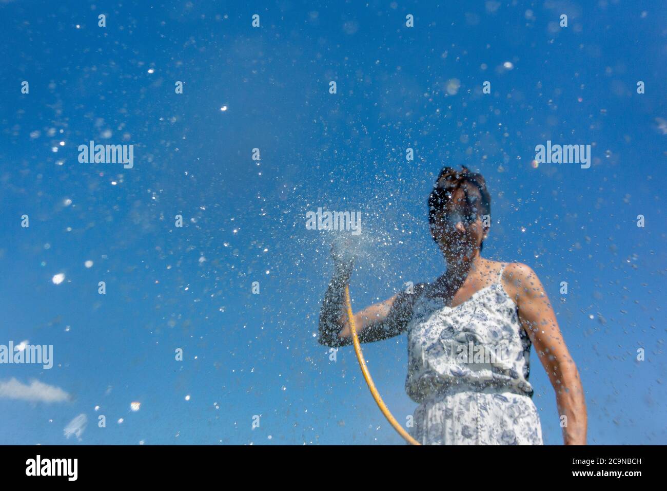 Woman spraying water from a hosepipe. North Yorkshire, UK. Stock Photo