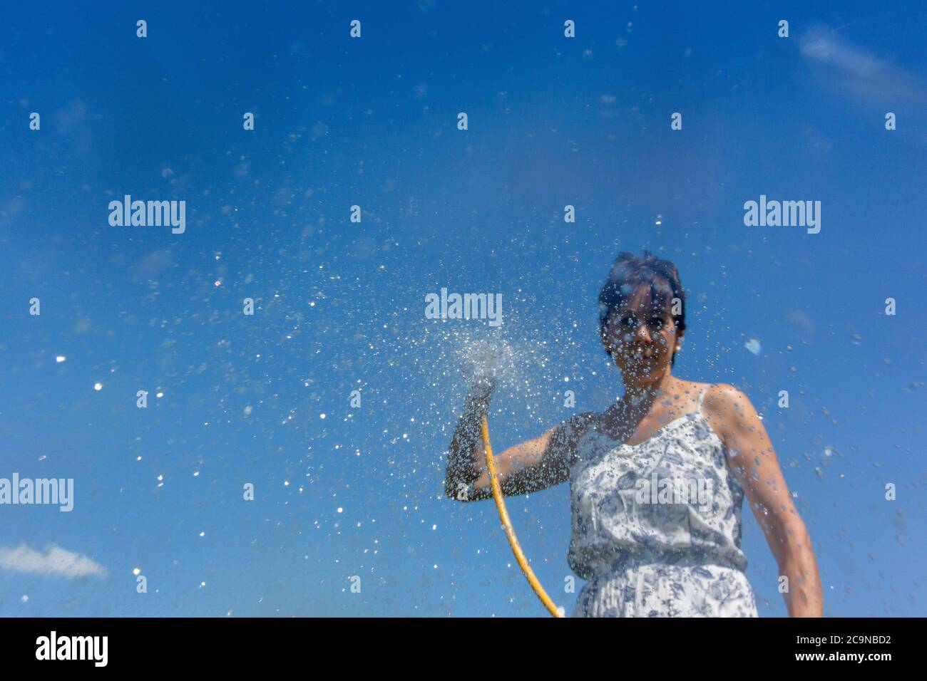 Woman spraying water from a hosepipe. North Yorkshire, UK. Stock Photo