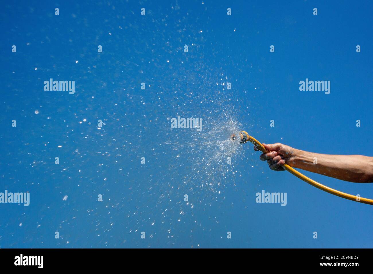 Water from a hose pipe being sprayed under pressure, against a blue summers sky. North Yorkshire, UK. Stock Photo