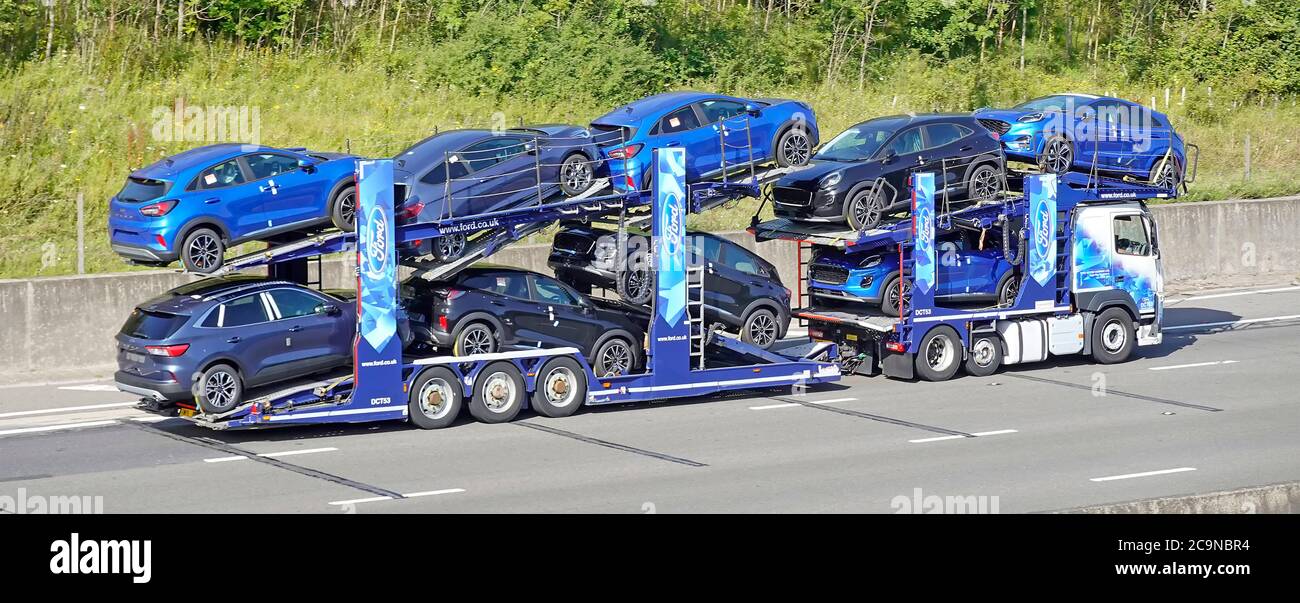 Ford motor company lorry truck car delivery transporter & trailer loaded with nine new unregistered blue cars driving UK motorway road Essex England Stock Photo