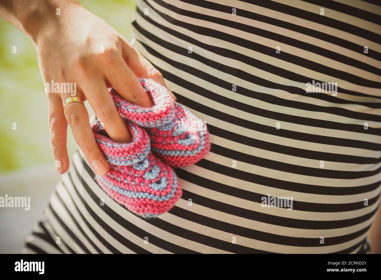 Close up portrait of happy pregnant woman holding small baby shoes, in summer park Stock Photo