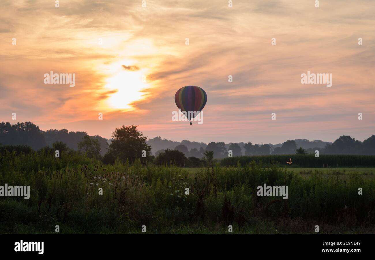 Hot Air Balloon floats over grass field and rolling hills at sunrise ...