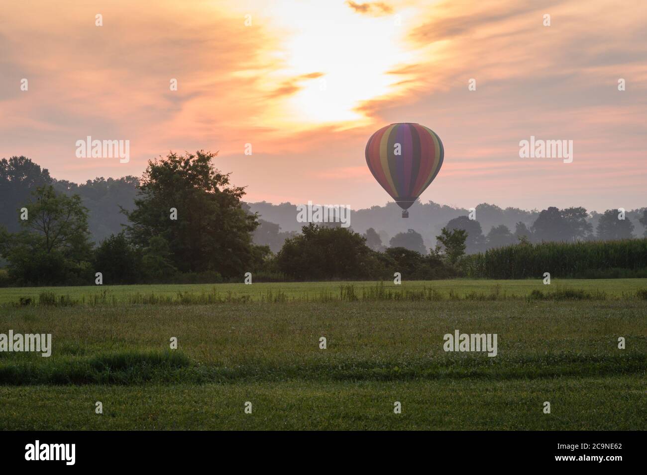 Hot Air Balloon floats over grass field and rolling hills at sunrise ...