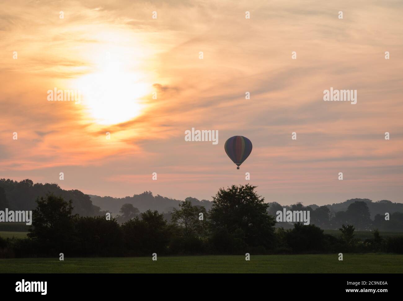 Hot Air Balloon floats over grass field and rolling hills at sunrise ...