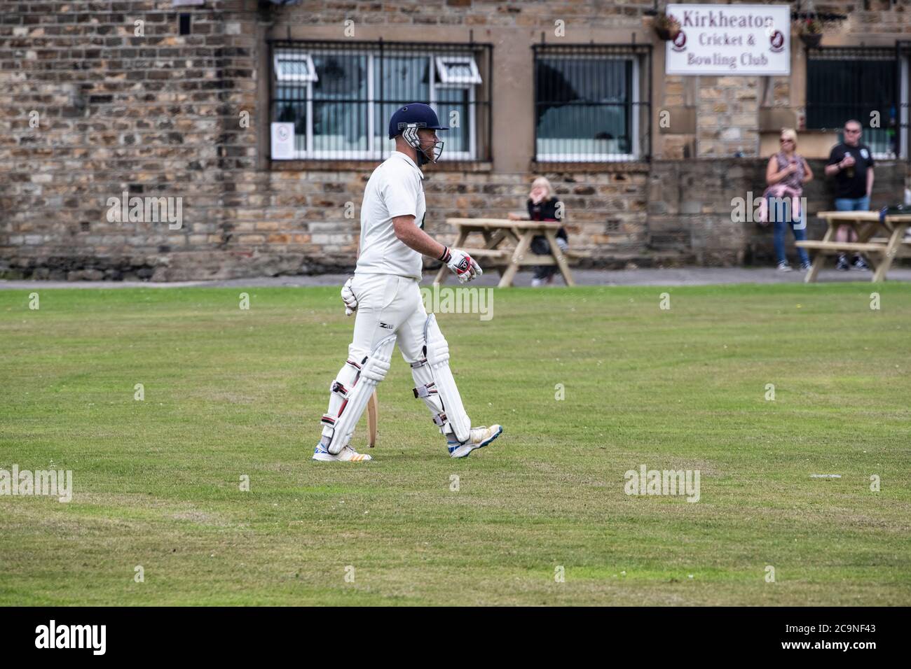 New Batsman in a village cricket match in West Yorkshire taking the field in pads, gloves and helmet with a cricket bat on a Saturday afternoon Stock Photo