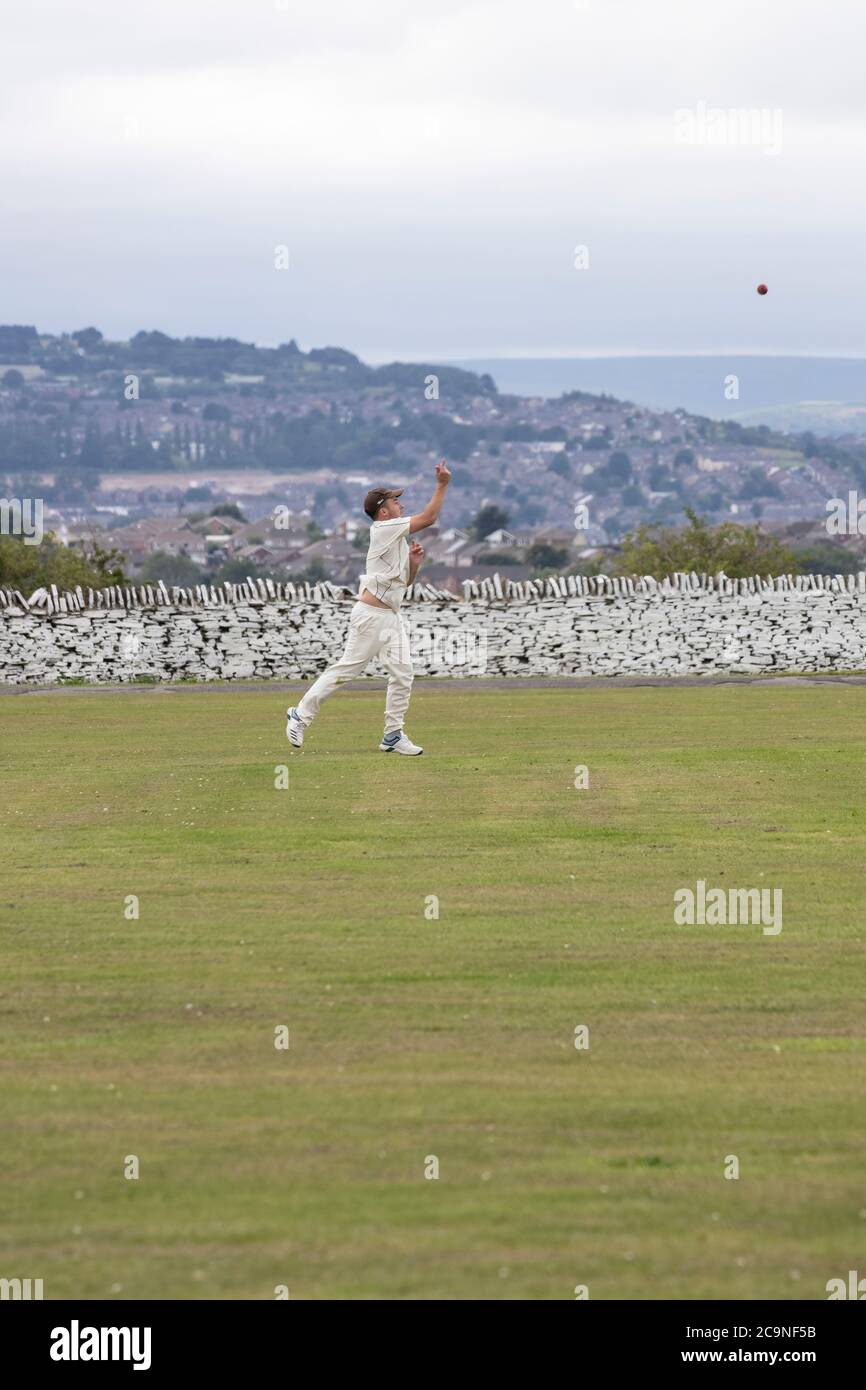 Cricket fielder in the outfield during a village cricket match throwing the ball back to the bowler Stock Photo