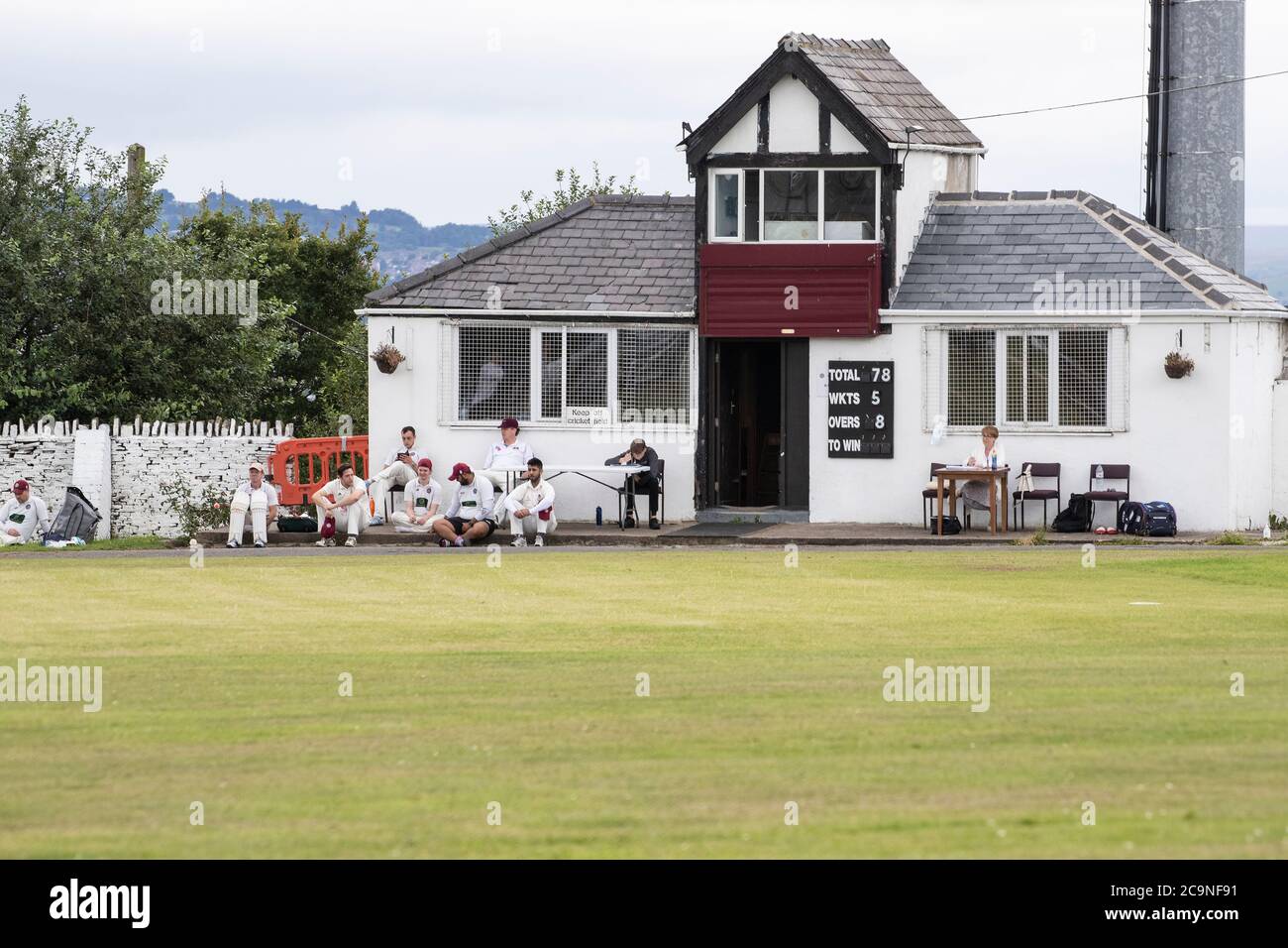 A cricket pavilion with the batting side and scorers watching the game in progress at a local village cricket match in West Yorkshire Stock Photo
