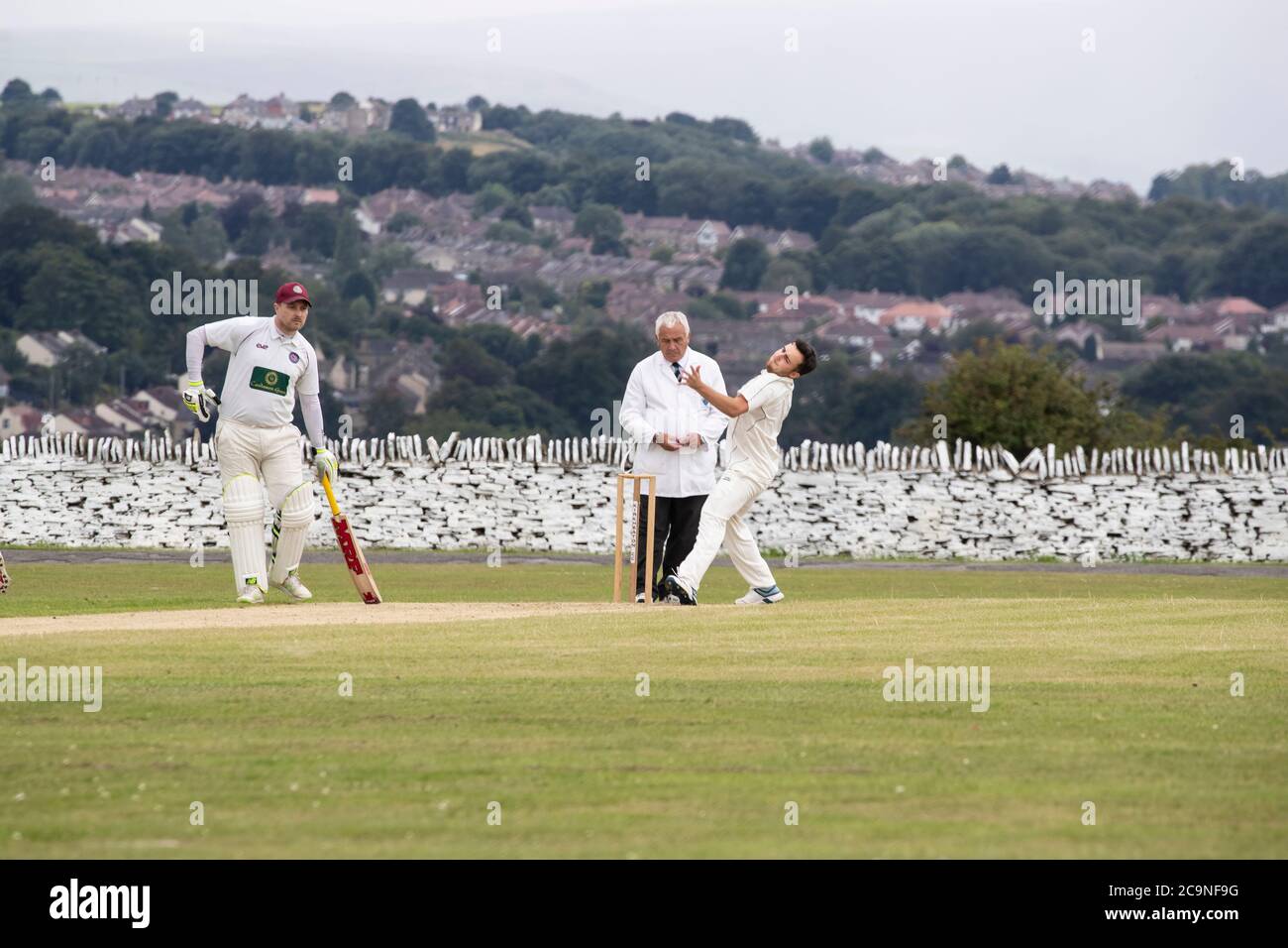 Bowler running past the umpire to bowl at a village cricket match in West Yorkshire U.K. Stock Photo